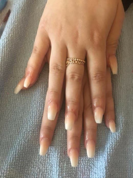 A fresh set of long nude ombre acrylic nails on a hand resting on a grey towel